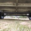 A close-up view of the underside of the Premium 8x5 Dual Axle Heavy Duty Tandem Trailer - 3200KG ATM, highlighting its axle and wheels, set on grass against a blurred background of park scenes with trees and pathways.