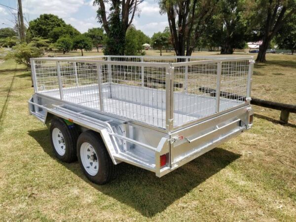 A Premium 8x5 Dual Axle Heavy Duty Tandem Trailer - 3200KG ATM For Sale, featuring galvanized metal mesh sides and white wheels, is parked on grass with trees and a blue sky in the background.