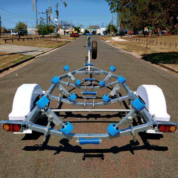 A 4.8m Galvanized Boat Trailer, perfect for boats 4.3-4.8m, sits on a paved road with trees and utility poles nearby. It features blue rollers and white fenders, situated in an urban area backdrop.