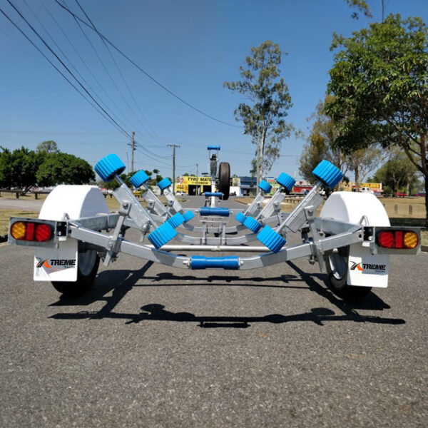 A 4.8m Galvanized Boat Trailer with blue rollers and white wheel fenders is on a paved road, with trees and streetlights visible in the background under a clear sky.