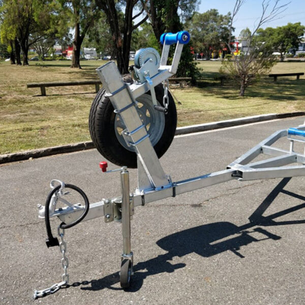 A 4.8m Galvanized Boat Trailer (750kg ATM), designed for 4.3-4.8m boats, is on an asphalt surface in a park. Featuring a hand winch, front-mounted spare tire, and securing chain, it sits amid trees and grass under a clear sky.