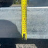 A yellow measuring tape stands upright against the metal surface of a Hydraulic Tipper Car Trailer with 3500KG ATM and a 16.4x6.6FT deck, marking around 100 cm. Its shadow appears on the metal, with part of a tire visible in the top left corner.