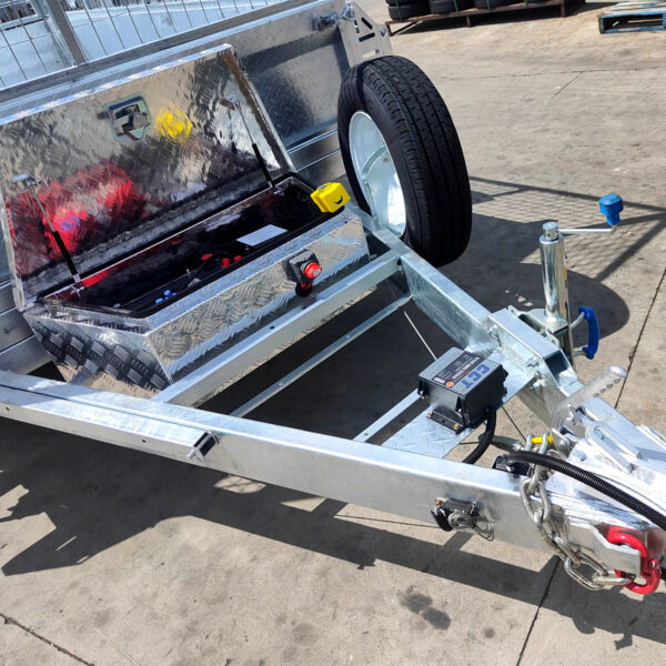 Close-up of the 8×5 Dual Axle Hydraulic Tipper Tandem Box Trailer (3500KG ATM) with an open storage box holding cables and tools, spare tire mounted on the side, and trailer hitch plus coupler on a concrete surface.