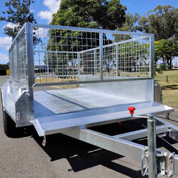 An 8×5 Single Axle Box Trailer ATM 1400KG with a jockey wheel and grid sides is parked on a paved surface, featuring a red handle on the front. Trees and grass are visible in the background under a partly cloudy sky.