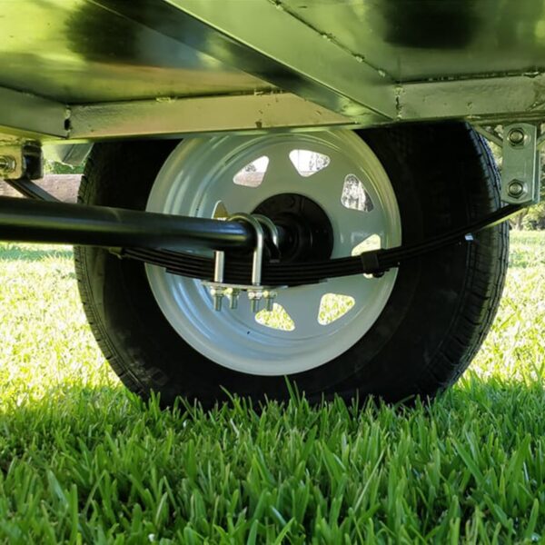 A close-up image shows the 8x5 Single Axle Box Trailer (ATM 750KG) with a jockey wheel on grass. The leaf springs and axle are connected by U-bolts to the tires white rim, revealing the metal undercarriage above.