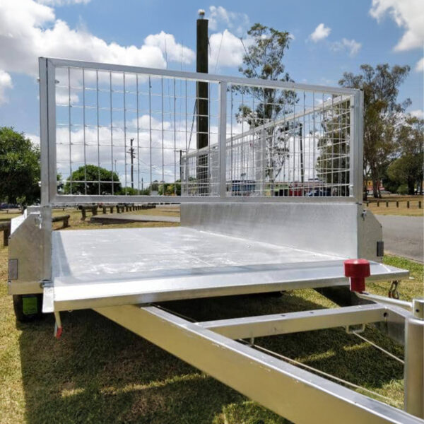 A Premium 8x6 Dual Axle Heavy Duty Tandem Trailer (2000KG ATM) is parked on grass near a road, with metal mesh sides, trees, and a partly cloudy sky in the background.