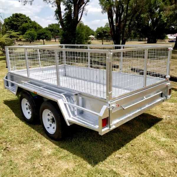 A Premium 8x5 Dual Axle Heavy Duty Tandem Trailer (3200KG ATM) with high mesh side panels is parked on grassy ground in a park-like area, surrounded by trees and a blue sky.