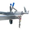 Close-up of a Premium 7x5 Single Axle Tradesman Trailer hitch with a lever and blue-capped knob, featuring an attached safety chain with pin. A supporting wheel appears at the bottom left against a plain white background.