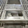 A close-up of the 8x4 Galvanized Plant Trailer For Sale - 3500KG ATM shows a metal grill with circular holes on either side and a rectangular center opening, partially covered by a flat metal plate, set against a textured metal surface background.