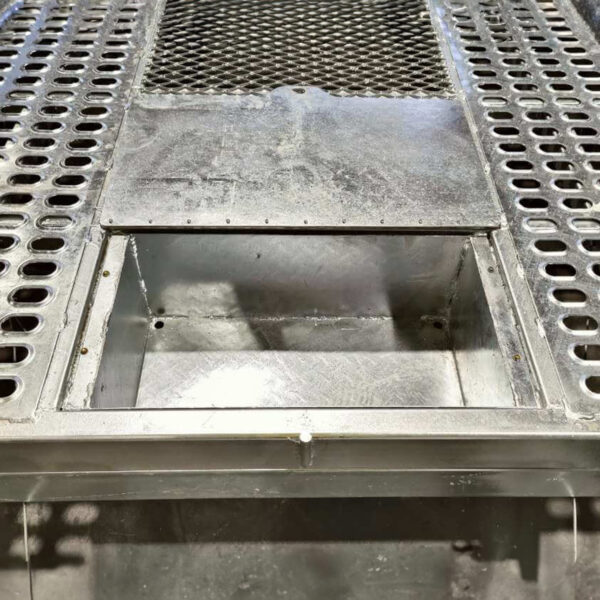 A close-up of the 8x4 Galvanized Plant Trailer For Sale - 3500KG ATM shows a metal grill with circular holes on either side and a rectangular center opening, partially covered by a flat metal plate, set against a textured metal surface background.