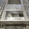 Industrial metal platform with a rectangular cutout in the center. The surface has perforated grids and a smooth section leading to an open compartment. The construction appears sturdy, with metallic textures prominent.
