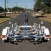 A 6.2m Galvanized Boat Trailer, suitable for 5.7m-6.2m boats, is parked on an empty road. The trailer features multiple wheel supports, a central spine, white fenders, and red tail lights, with trees and electrical poles lining the street in the background.