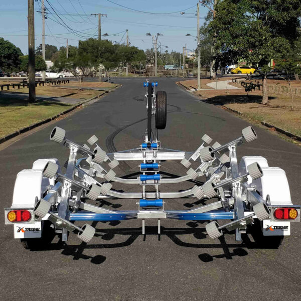 A 6.2m Galvanized Boat Trailer, suitable for 5.7m-6.2m boats, is parked on an empty road. The trailer features multiple wheel supports, a central spine, white fenders, and red tail lights, with trees and electrical poles lining the street in the background.