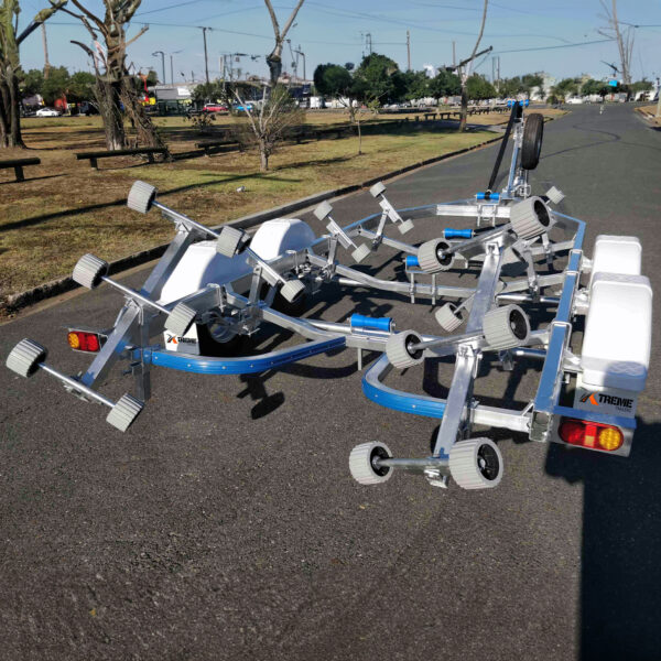 A 6.2m Galvanized Boat Trailer with 2000kg ATM, perfect for 5.7m-6.2m boats, features adjustable supports and wheels, decorated with white and blue elements plus reflectors. Its parked on a paved road near a park filled with trees and benches under a clear blue sky.