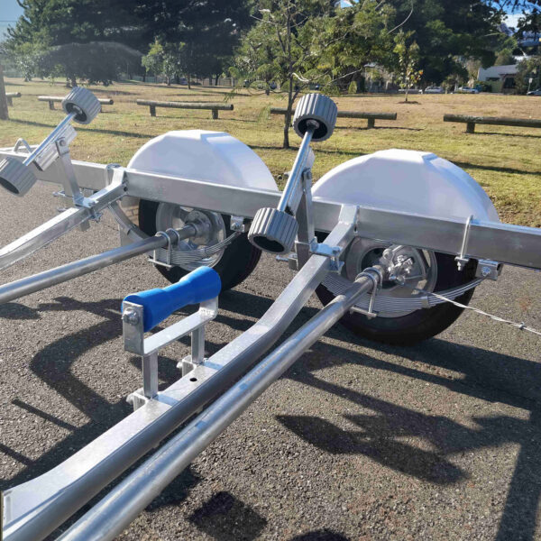 A 6.2m Galvanized Boat Trailer with 2000kg ATM, perfect for boats 5.7m-6.2m, is parked on pavement in a park. It features two large wheels and adjustable supports, with grass and trees under a clear blue sky in the background.
