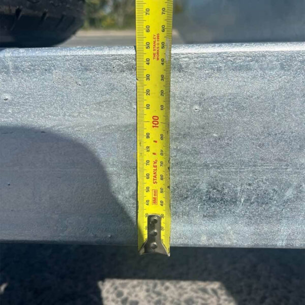 A 7.5m Galvanized Dual Axle Boat Trailer with 3500kg ATM, perfect for boats from 6.8m to 7.5m, is shown with a yellow tape measure vertically against its slightly weathered surface, indicating around 100 cm. A shadow and part of a wheel are visible in the background.