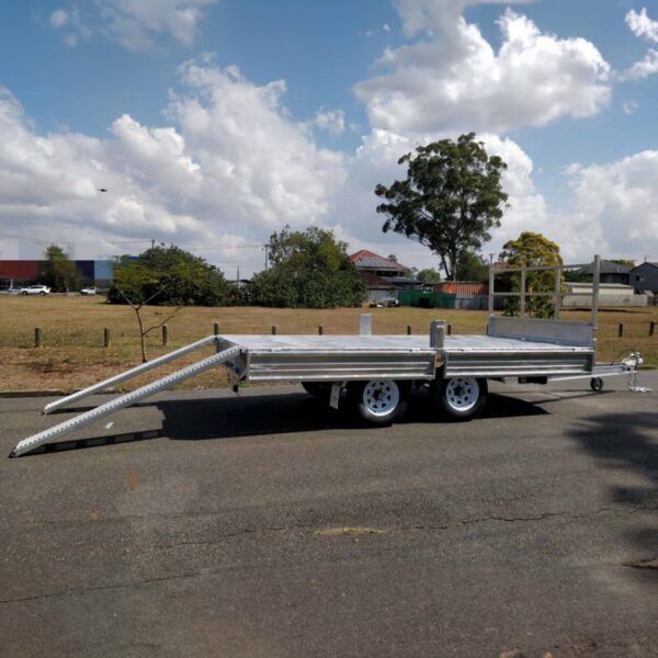 A Premium 14x7 Galvanized Flat Top Trailer with 3500KGS ATM and Ramps is parked on a paved road. The backdrop features partly cloudy skies, trees, a fence, and buildings.