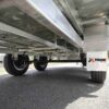 View from beneath a Premium 14x7 Galvanized Flat Top Trailer with 3500KGS ATM and Ramps, showing its undercarriage and wheels on a paved road. The Xtreme Trailers logo is visible on the side.