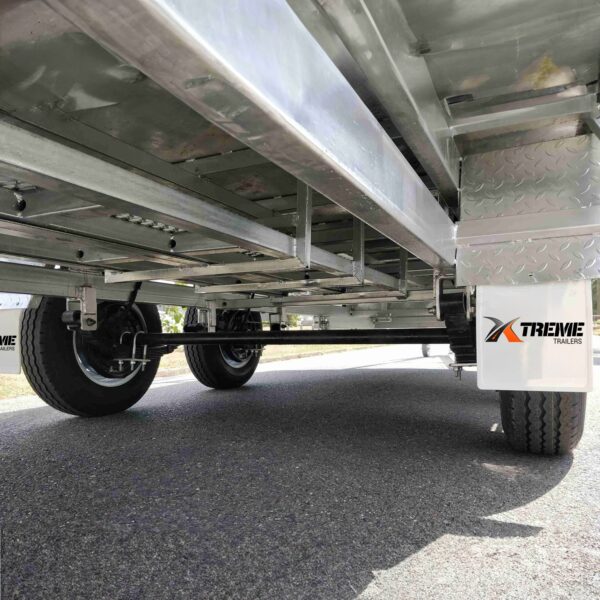 View from beneath a Premium 14x7 Galvanized Flat Top Trailer with 3500KGS ATM and Ramps, showing its undercarriage and wheels on a paved road. The Xtreme Trailers logo is visible on the side.