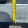 A measuring tape is vertically positioned against a metallic surface of the 14×7 Dual Axle Hydraulic 3-Way Tipper Flat Top Trailer - 3500KG ATM with Ramps, reading just over 90 centimeters. A shadow is cast on the textured ground in the background.