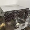 The 3.8m Big Box Food Trailer features a silver metallic exterior with a diamond plate pattern, secured by a latch and lock. Resting on its matching industrial surface, it boasts a side circular vent with horizontal slats.