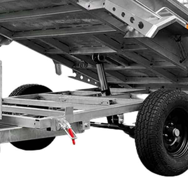 Close-up of the 8x5 Hydraulic Tipper Single Axle Box Trailer ATM 1800kg. Features a tilting bed lifted by a hydraulic piston, large black wheels, sturdy frame, and a red safety latch near the hitch.