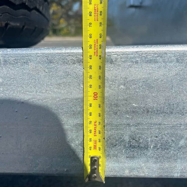 A yellow measuring tape is extended vertically against the 14x7 Dual Axle Hydraulic Tipper Tandem Box Trailer - 4500KG ATM With Ramps, showing a 100 cm measurement at the top edge. A tire and a blurred outdoor background are partially visible.