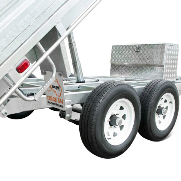 Close-up of the Premium 12×7 Hydraulic 3-Way Tipper Galvanised Flat Top Trailer (4500kg ATM, Pre-order), featuring its dual-axle design with two visible wheels, a sturdy metal toolbox, and a phone number displayed on the frame. The hydraulic tipper tray is shown partially raised.
