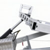 Close-up of the Premium Hydraulic Tipper Car Trailer 4200kg ATM 16.4x6.6FT (5x2M) Deck Size - Punched Floor (Pre-order), showcasing its mechanical hydraulic system with a metal piston, connecting rods, and a textured metal box with attached hoses, all set against a plain white background.