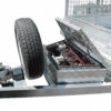 Close-up of the 8×5 Dual Axle Hydraulic Tipper Tandem Box Trailer 3200kg ATM (Pre-order) showing its metal frame with a mounted spare tire and an open toolbox revealing the battery and internal wiring. The surface is finished with a diamond plate pattern.